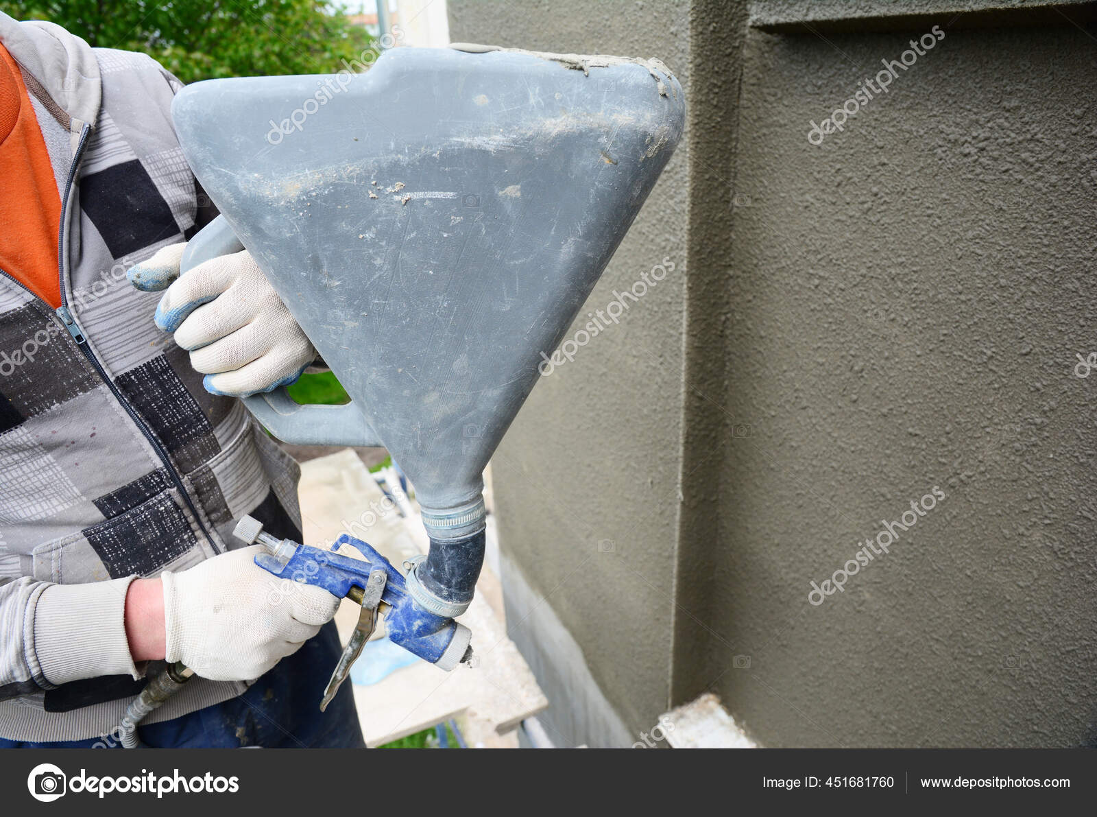 A building contractor is renovating, rendering exterior walls of the house, applying stucco, spaying texture using a texture air spray gun.